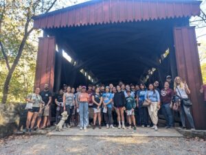 Large group of teens and adults standing in front of a covered bridge